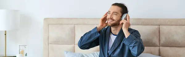 Un hombre se sienta en una cama, se dedica a la música en sus auriculares. - foto de stock