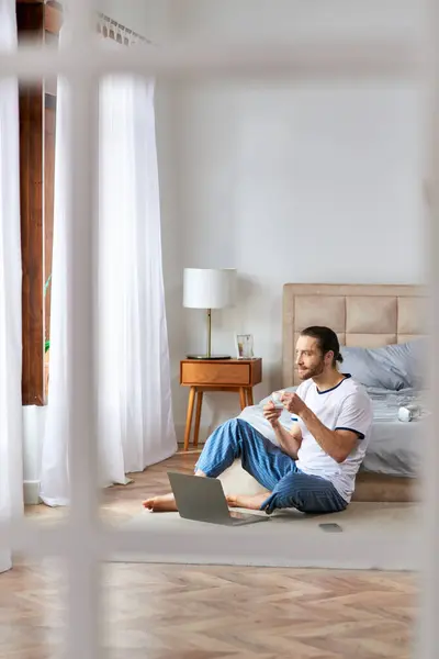 A man, surrounded by serenity, drinking coffee while using a laptop on the floor. — Stock Photo
