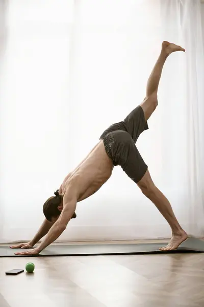 Hombre guapo en una pose de yoga junto a una ventana en casa. - foto de stock