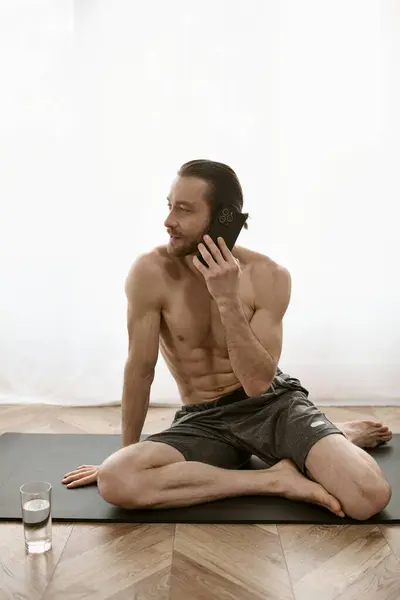Bonito homem no tapete de ioga conversando no celular durante a rotina da manhã. — Fotografia de Stock