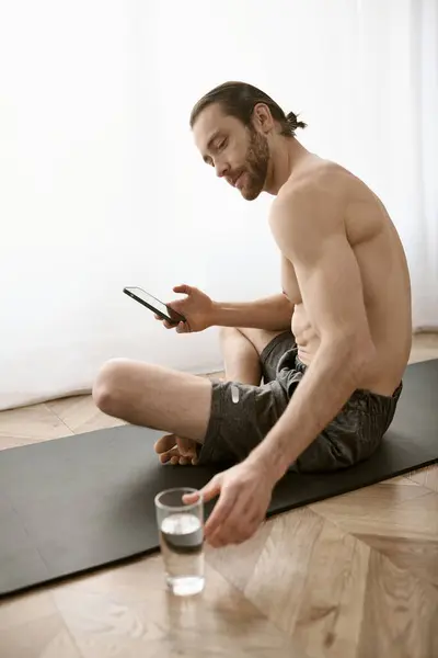 Shirtless man on yoga mat, engrossed in phone. — Stock Photo