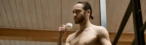 Un uomo senza camicia tiene in mano una tazza bianca. — Foto stock