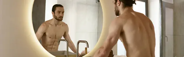 Un hombre se para ante un espejo de baño para su rutina de cuidado de la piel matutina. - foto de stock