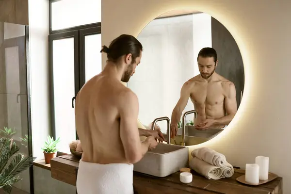Um homem está diante de um espelho do banheiro, engajando-se em sua rotina matinal de cuidados com a pele. — Fotografia de Stock