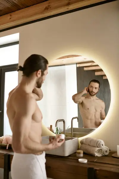 Un hombre se para frente a un espejo del baño, dedicándose a su rutina de cuidado de la piel matutina. - foto de stock