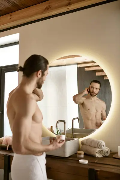 Un uomo si trova davanti a uno specchio del bagno, impegnato nella sua routine di cura della pelle del mattino. — Foto stock