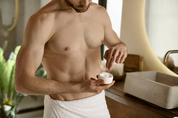 Un hombre en una toalla aplicando crema. - foto de stock