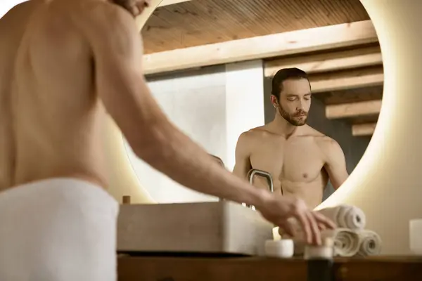 Un bel homme en sous-vêtements blancs se tient devant un miroir, s'engageant dans une routine de soins de la peau. — Photo de stock