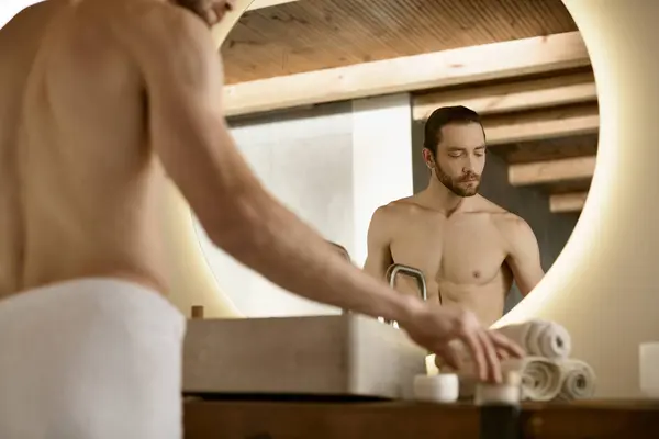 Bello uomo in biancheria intima bianca sta davanti a uno specchio, impegnandosi nella routine di cura della pelle. — Foto stock