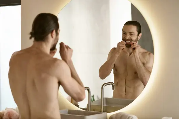 Un uomo che si lava i denti davanti allo specchio, parte della routine mattutina di cura della pelle. — Foto stock