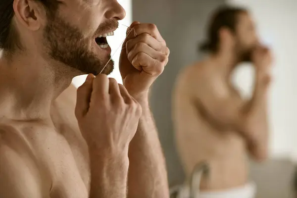 Um homem com um rosto bonito escova os dentes na frente de um espelho. — Fotografia de Stock