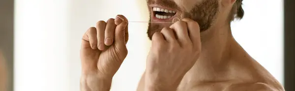 Un homme torse nu se brosse les dents devant le miroir, ce qui fait partie de sa routine matinale. — Photo de stock