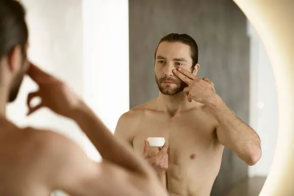 Um homem aplicando creme na frente de um espelho durante sua rotina matinal. — Fotografia de Stock
