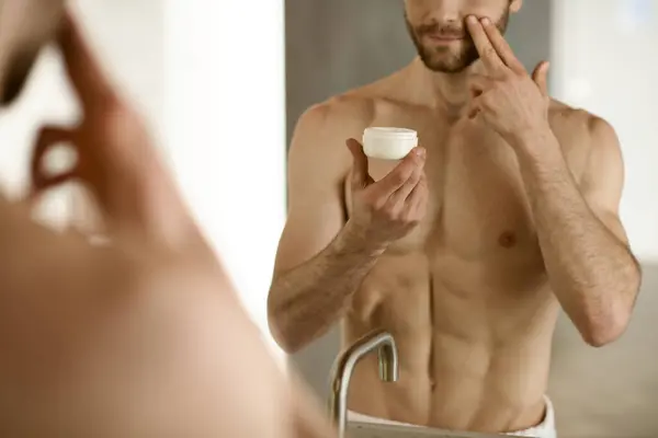Un uomo che applica la crema davanti a uno specchio durante la sua routine mattutina. — Foto stock