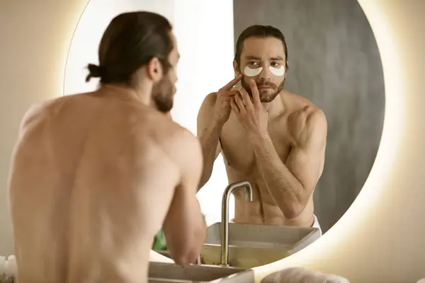 A handsome man applying patches in front of a mirror during his morning skincare routine. — Stock Photo