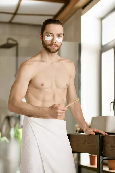 Handsome man with towel around waist conducts morning skincare routine. — Stock Photo