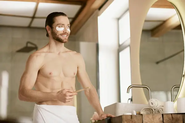 Un uomo in asciugamano, che fa la routine mattutina di cura della pelle, in piedi davanti allo specchio. — Foto stock