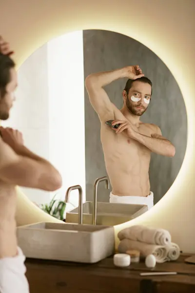 Ein Mann mit Handtuch steht vor einem Spiegel und übt sich in seiner Morgenpflege. — Stockfoto