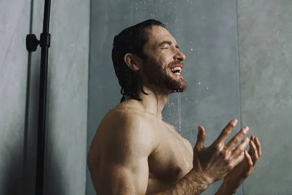 Bell'uomo in piedi sotto la doccia con le braccia alzate, parte della sua routine mattutina. — Foto stock