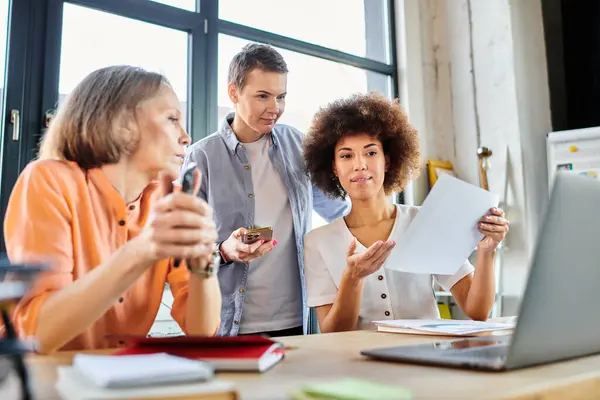 Groupe diversifié de femmes d'affaires rassemblées autour d'un ordinateur portable dans un espace de coworking. — Photo de stock