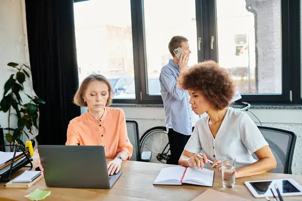 Hard-working, diverse female professionals collaborate around a table with laptops in a modern office setting. — Stock Photo