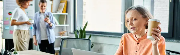 A woman enjoys her coffee as she works on her laptop next to her diverse colleagues. — Stock Photo