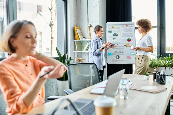 Two businesswomen discussing ideas on whiteboard in office, with their mature colleague in front of them. — Stock Photo