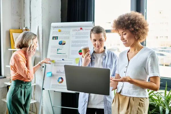 Diverse group of hard-working businesswomen standing around a laptop in a coworking space. — Stock Photo