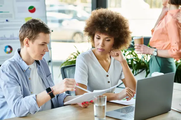 Diverse businesswomen sit together at a table, focusing on paperwork and discussing business matters. — Stock Photo
