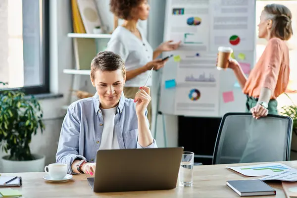 Attraktive Geschäftsfrau vertieft in die Arbeit am Laptop, mit ihren vielfältigen Kollegen im Hintergrund. — Stockfoto