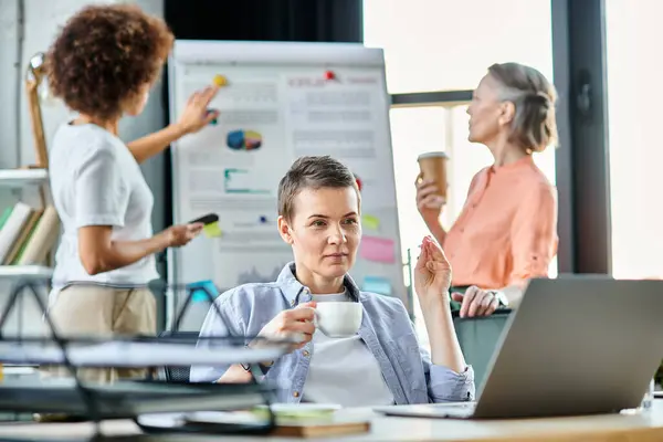 Attenta donna d'affari assorta nel lavoro su un computer portatile, con i suoi diversi colleghi sullo sfondo. — Foto stock