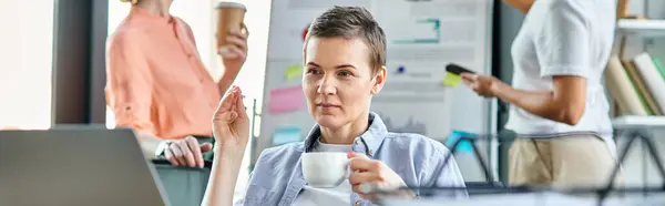 Dedicated businesswoman engrossed in work on a laptop computer, with her diverse colleagues on backdrop. — Stock Photo