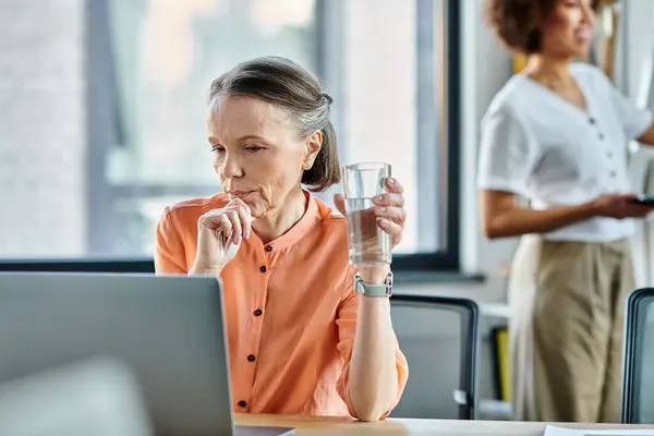 Посвящённая женщина сосредоточилась на ноутбуке, погрузилась в работу в современном офисе, со своим африканским американским коллегой на заднем плане. — стоковое фото
