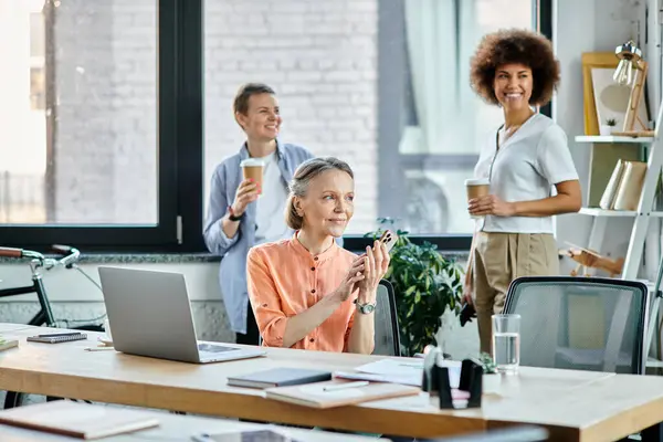 Mulher de negócios alegre falando ao telefone enquanto usa laptop, com seus diversos colegas em pano de fundo. — Fotografia de Stock