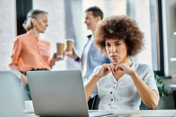 Young african american businesswoman using laptop, with her diverse colleagues on backdrop. — Stock Photo