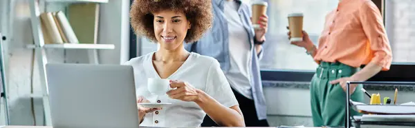 Appealing african american businesswoman using laptop, with her diverse colleagues on backdrop. — Stock Photo