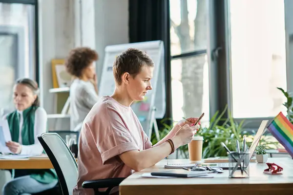 Short haired woman engrossed in work, with phone, with her diverse colleagues on backdrop. — Stock Photo