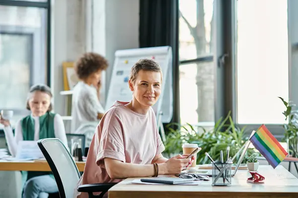 Cheerful woman engrossed in work, with phone, with her diverse colleagues on backdrop. — Stock Photo