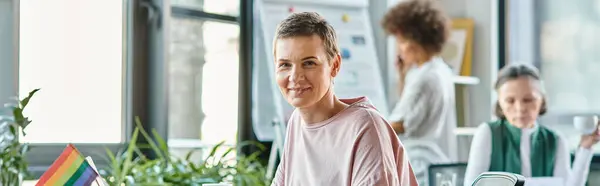 Jolly woman engrossed in work, with her diverse colleagues on backdrop. — Stock Photo