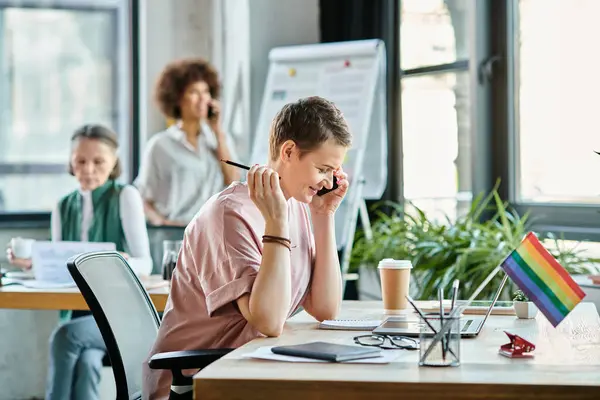 Hard working woman engrossed in work, with phone, with her diverse colleagues on backdrop. — Stock Photo