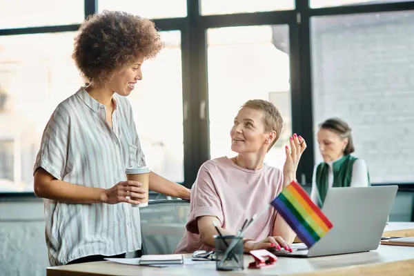 Cheerful diverse businesswomen working together on project in office, pride flag. — Stock Photo