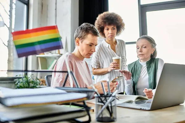 Уважні різноманітні бізнесмени, в тому числі члени ЛГБТ-спільноти, інтенсивно працюють навколо ноутбука в офісі. — стокове фото