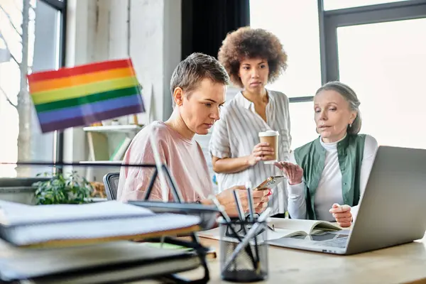 Attentive diverse businesswomen, including members of the LGBT community, working intently around a laptop in an office. — Stock Photo