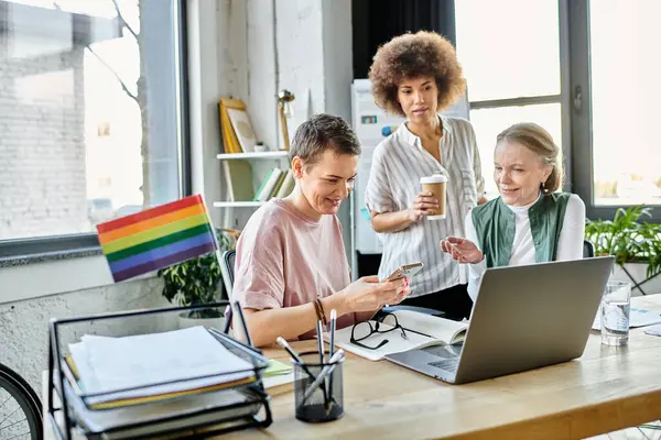 Joyous diverse businesswomen, including members of the LGBT community, working intently around a laptop in an office. — Stock Photo