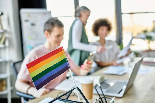 Focus on rainbow flag displayed on office table in front of blurred dverse businesswomen. — Stock Photo