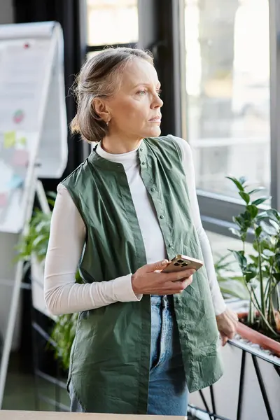 Женщина, элегантно стоящая у окна, взаимодействует со своим мобильным телефоном. — стоковое фото