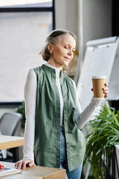 Une femme d'affaires élégante profite d'une tasse de café dans son cadre de bureau. — Photo de stock