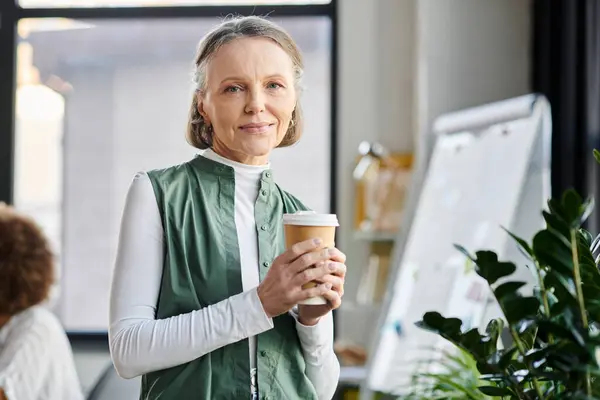 Businesswoman holds a coffee cup and looking at camera. — Stock Photo