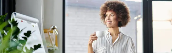 African american woman standing by a window, holding a cup. — Stock Photo