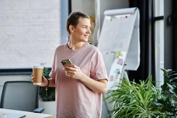 Una mujer profesional multitarea con una taza de café y teléfono celular. - foto de stock